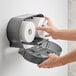 A person's hands putting a roll of toilet paper into a Lavex Black double roll toilet tissue dispenser.