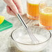 A hand using an American Metalcraft stainless steel mini bar whisk to stir a bowl of white liquid.