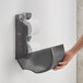 A hand holding a black Lavex double roll vertical toilet tissue dispenser with toilet paper on it.