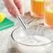 A hand using an American Metalcraft stainless steel mini bar whisk to stir a bowl of lemonade.