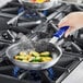 A hand holding a Vollrath Wear-Ever frying pan filled with food on a stove with steam coming out.