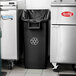 A black Lavex rectangular under-counter trash can in a kitchen next to a silver refrigerator.