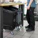 A man standing next to a Lavex black rectangular under-counter trash can.