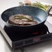 A black carbon steel fry pan with a steak cooking inside, placed on an induction cooktop.