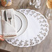 A person holding a plate with a Hoffmaster lace doily, a fork, and a glass of wine.