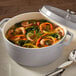 A gray non-stick round casserole dish with a cover, filled with shrimp and vegetable soup.