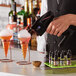 A hand holding a black Flavour Blaster machine over a cocktail glass with orange liquid inside.