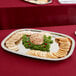 An Elegant Reflections stainless steel oblong serving tray with crackers and a ball of cheese on a table.