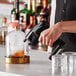 A person using a Flavour Blaster cocktail aroma machine to smoke a drink in a glass on a counter.