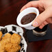 A person holding a small white Thunder Group fluted ramekin of brown sauce.