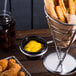 A stainless steel American Metalcraft cone basket filled with fried food next to 2 ramekins of sauce on a table.