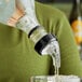 A person using a white Choice 3-Ball Measured Liquor Pourer to pour liquid into a glass on a table.