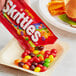 A hand holding a SKITTLES® Original Fruity Candies pouch.