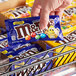 A hand holding a small package of M&M's Caramel Milk Chocolate Candies.