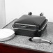 A rectangular metal chafer with chrome accents on a marble counter top.