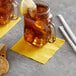 A glass mug with a yellow Choice cocktail napkin and a lemon slice on top of it next to a cookie.