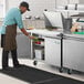 An apron and gloved man prepares food on an Avantco sandwich prep table in a professional kitchen.