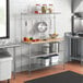 A Regency stainless steel baker's rack with a hardwood cutting board on a shelf in a kitchen.