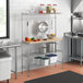 A Regency chrome wire shelf with a hardwood cutting board on a kitchen counter with utensils.