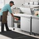 A man in an apron using an Avantco stainless steel refrigerator to prepare sandwiches.