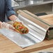 A person in gloves holding a hot dog on EcoChoice aluminum foil.