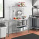 A Regency baker's rack with metal and stainless steel shelves and a plastic cutting board on a kitchen counter.