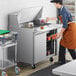 A man using an Avantco stainless steel sandwich prep table to prepare food in a commercial kitchen.