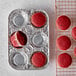 A red cupcake with a white wrapper in a D&W Fine Pack foil muffin pan on a wire rack.