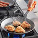 A person using a Lodge carbon steel frying pan to cook chicken.