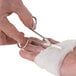 A person using Medique wire scissors to cut a bandage on a hand.