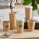 A person pouring coffee into a brown New Roots compostable paper cup with a translucent lid.