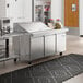 An Avantco stainless steel sandwich prep table on a large stainless steel counter top in a commercial kitchen.