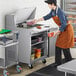 A man in an apron using an Avantco stainless steel sandwich prep table to put food in a container.