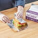 A person wearing gloves is wrapping a sandwich in Choice interfolded foil sheets.