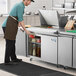 A man in a kitchen using a white rectangular commercial sandwich prep table.