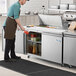 A man in a brown apron using an Avantco stainless steel sandwich prep refrigerator to store food.