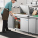 A man preparing food on an Avantco stainless steel sandwich prep table in a professional kitchen.