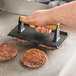 A person using an American Metalcraft cast iron steak weight to press a hamburger patty.