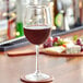 An Acopa Select Flora wine glass filled with red wine on a table with a coaster.