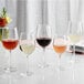 A white table with a group of Acopa Select Flora wine glasses filled with red, white, and pink wine.