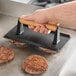 A person using an American Metalcraft steak weight to cook hamburgers on a grill.