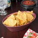 A raspberry polyethylene oval basket filled with tortilla chips on a table in a Mexican restaurant.