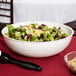 A white Camwear round ribbed bowl filled with salad on a table.