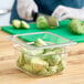 A person cutting up brussels sprouts in a Cambro plastic food pan on a counter.