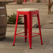 A red Lancaster Table & Seating outdoor backless counter height stool with a tan cushion on top.