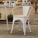 A Lancaster Table & Seating white outdoor arm chair with a tan cushion on a patio.