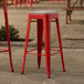 A red Lancaster Table & Seating outdoor barstool with a gray cushion on a stone surface.