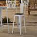 A Lancaster Table & Seating white outdoor cafe barstool with a black cushion on a table.