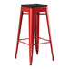 A red metal Lancaster Table & Seating outdoor backless barstool with a black cushion.