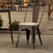 A Lancaster Table & Seating copper outdoor cafe chair with a tan cushion on a patio.